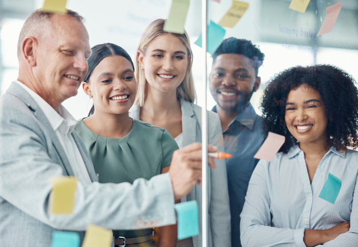 Team, strategy and business people writing on sticky notes in a meeting about the vision, mission and goals of the company. Teamwork, smile and happy group of employees brainstorming in modern office