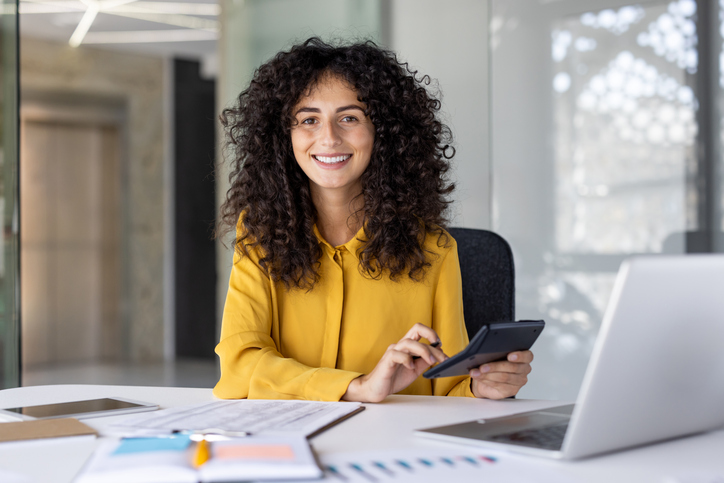 Successful financier accountant at workplace inside office. Businesswoman behind paperwork smiling and looking at camera. Satisfied female office worker, with graphs and charts.