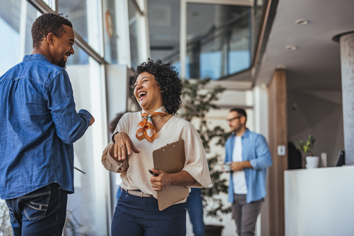 Two coworkers enjoy a lighthearted moment in a bright, modern office environment, conveying teamwork and positivity. The casual atmosphere suggests a collaborative and friendly workplace.